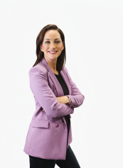 Viktoria, ehrenamtliche Abteilungsleiterin Rollkunstlauf beim Verein BTV Wuppertal, mit verschränkten Armen im fliederfarbenen Blazer vor weißem Hintergrund